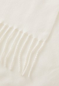 Écharpe en laine blanche avec des bords à franges. La texture semble douce et texturée, avec un motif subtil. Les franges sont régulièrement espacées le long d'un bord.