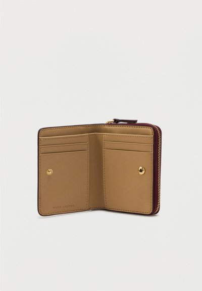 Tan leren portemonnee met een bordeauxrode rits. Bevat twee kaartsleuven, een gouden drukknoop en een gegraveerd merklogo aan de binnenkant.