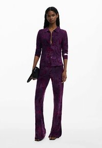 Paarse blouse met bloemenpatroon, knoopsluiting en lange mouwen, gecombineerd met bijpassende wijde broek. Gladde stoftextuur, nauwsluitende pasvorm.