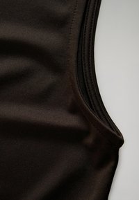 Close-up of black sleeveless fabric with visible seam stitching and fine textured weave on a light background.