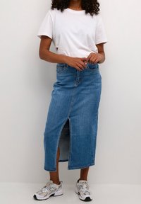 Falda larga vaquera con una abertura frontal, tono azul y cinturilla estándar. Combinada con una camiseta blanca lisa y zapatillas grises.