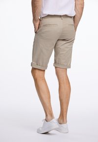 Beige puuvillashortsit, joissa on käännetyt lahkeet, takataskut ja sileä pinta, yhdistettynä valkoisiin vaeltajakenkiin.