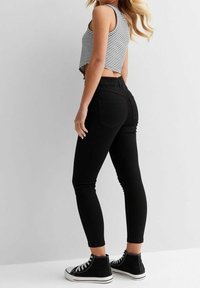 Black skinny jeans with back pockets, paired with a striped crop top and high-top sneakers. The fabric appears smooth with a fitted silhouette.