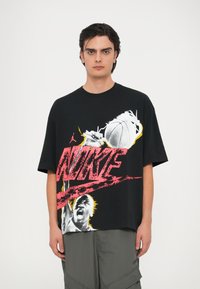 Must have ja suurusega must T-särk, millel on erksad punased ja kollased graafilised printimised ning tekst "NIKE" koos korvpalli motiiviga. Valmistatud puuvillast, lühikeste varrukatega.