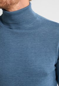 Suéter de cuello alto azul, acanalado, hecho de una suave tela de punto. Diseño ajustado con un alto cuello y una textura suave, adecuado para capas.