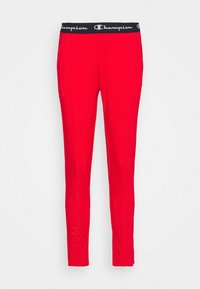 Röda idrottsbyxor med svart elastisk midja som har Champion-logotypen. Slät textur och slim fit som sträcker sig ner till anklarna.