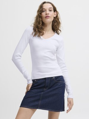 Witte lange mouw top met V-hals, gecombineerd met een donker denim minirok met vijf-pocket styling en contraststiksels.