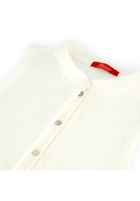 Natural fiber sleeveless top in off-white with button closure, featuring a subtle embossed pattern and light blue buttons. Red brand label visible.