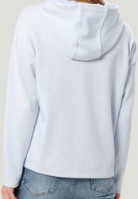 Hoodie bleu clair avec une finition texturée, muni d'une capuche à cordon de serrage et de manches longues. Design simple avec une coupe décontractée et sans embellissements visibles.
