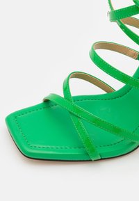Sandalo verde con cinturini e punta quadrata, caratterizzato da cinturini in pelle lucida e suola piatta, dettagliato con cuciture a contrasto.
