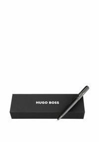 Schwarzer Hugo Boss-Stift mit strukturierter Griffoberfläche, platziert auf einer schwarzen Box, die den Markennamen in Weiß zeigt. Elegantes, minimalistisches Design.