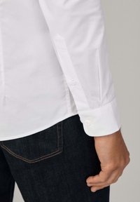 Witte langemouwen shirt met knoopscharen, getoond met donkere spijkerbroek. Glad stof met een klassieke snit en op maat gemaakte details.