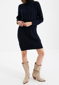 Námořnický pletený svetr ve stylu šatů s rolákem, kabelovým vzorem a žebrovanými detaily, spárovaný se světle béžovými kotníkovými botami s mírn�ým podpatkem.