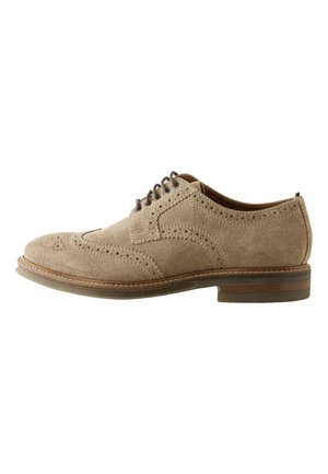Jasnobrązowy zamszowy męski but brogue z detalami wingtip, zamkniętym sznurowaniem, perforowanymi wzorami oraz piętą nałożoną warstwowo na białym tle.
