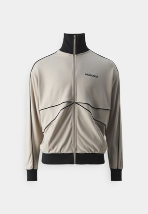 Beige zip-up jacket with black accents, stand collar, and side pockets; features curved seam lines and "FRANCHISE" logo on the chest.