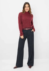 Bordeaux coltrui met marineblauwe, gestreepte broek met wijde pijpen, bevestigd met een bijpassende riem. Glanzende bordeaux punten schoenen.