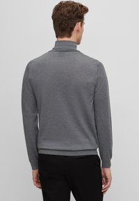 Pull-over gris à manches longues avec un col montant, présentant une texture lisse et un ourlet ajusté. Design simple et polyvalent.