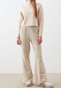 Beige dvoudílný outfit skládající se z kratšího roláku a rozšířených kalhot. Měkká látka s podrobnými švy. Boty mají masivní podrážku.