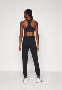 Schwarze Sport-BH mit Racerback-Design, kombiniert mit schwarzen Jogginghosen mit Rippbündchen, getragen mit weißen Sportschuhen.