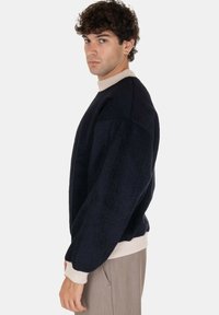 Maglione blu navy con maniche larghe e morbide e collo a costine di un leggero beige. Presenta un tessuto testurizzato e polsini elasticizzati all'orlo.