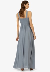 Maxikleid aus weich blauem Stoff, mit gerafftem Oberteil, breiten Trägern und einem schwingenden Rock. Leicht und mit glatter Textur.