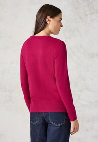 Fuchsia Strickpullover mit rundem Halsausschnitt, gerippten Bündchen und Saum sowie einer glatten Textur. Getragen mit dunkelblauen Jeans.