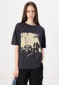Černé oversized tričko s retro potiskem auta a postav proti světlému pozadí. Měkký bavlněný materiál.