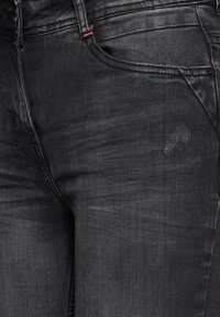 Svarta denimjeans med en lätt blekt struktur, framfickor och subtila stickningsdetaljer i röd närheten av midjebandet.