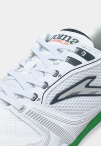 Fehér sportcipő hálós panelekből, világoskék fűzőkkel és zöld talppal. Jellemzője egy szürke logó és finom csíkos díszítés az oldalon.