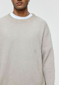 Beige geribde gebreide trui met een ronde hals. Lange mouwen en een relaxte pasvorm. Subtiele textuur met een lichte variatie in tint.