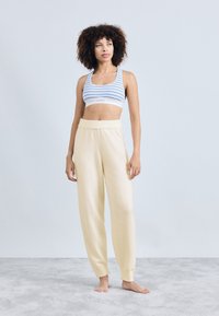 Pantalones de forro polar de color amarillo claro con un ajuste relajado y cintura elástica, combinados con un top corto a rayas azul y blanco. Textura suave, diseño casual.