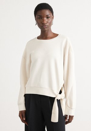 Lichtbeige sweatshirt gemaakt van zachte stof, met een zij-knoopdetail en een relaxte pasvorm, met verlaagde schouders en een ronde halslijn.
