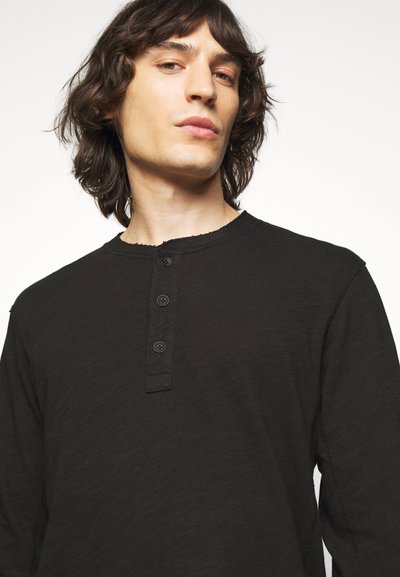 Black long-sleeve shirt with a round neckline, featuring a three-button placket, textured fabric, and raw edge detailing along the collar.
