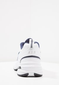 Zapatilla deportiva blanca con detalles en azul marino, tejido texturizado y logo "AIR" en el talón. Presenta una tira de pull tab a rayas y una suela acolchada.