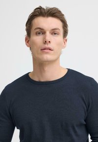 Marineblauwe trui met ronde hals, gemaakt van een gladde gebreide stof en voorzien van geribbelde manchetten. Eenvoudig ontwerp, zonder patronen of zichtbare hardware.