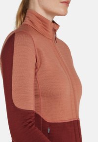 Chaqueta de forro polar con un alto cuello en un degradado de color durazno a burdeos, con cremallera frontal y un acabado texturizado.