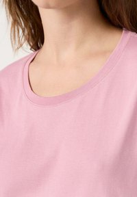Camisa de manga corta rosa con un amplio escote en pico y una suave textura de algodón, con costuras sutiles a lo largo de los bordes.