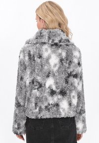 Chaqueta recortada de pelaje gris y blanco con un patrón texturizado, cuello ancho y mangas largas, vista desde la parte posterior.