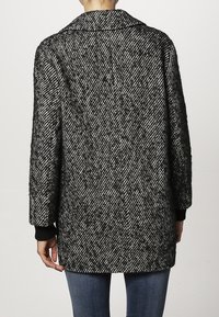 Abrigo de patrón de espiga en blanco y negro con un cuello estructurado, corte holgado y puños acanalados. Tela texturizada con un aspecto suave.
