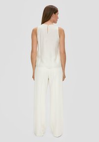 Weißes ärmelloses Top mit einem Schlüsselverschluss auf der Rückseite, kombiniert mit weiten weißen Hosen. Der Stoff wirkt glatt und leicht.