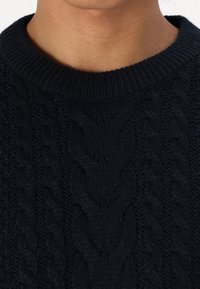 Suéter de punto en navy oscuro que presenta un patrón de punto trenzado y un cuello redondo acanalado. La textura es gruesa y texturizada, lo que garantiza calidez.