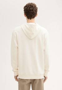 Kremowa bluza z kapturem z elastycznymi mankietami i dołem. Miękka tekstura, prosty design i luźny krój. Widok z tyłu.