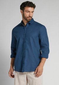 Mans långärmad skjorta i mörkblått, tillverkad av texturerad tyg, med knäppning fram och uppvikt ärmar.