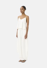 Witte tweedelige outfit met een cropped top met spaghettibandjes en losse, brede broek. Lichte stof met een subtiele textuur.