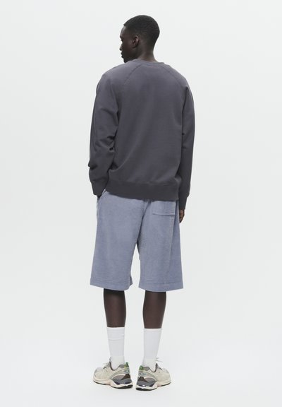 Dunkelgrauer Sweatshirt mit geripptem Saum und Bündchen, kombiniert mit hellblauen Cordshorts mit seitlicher Tasche. Graue Sneakers und weiße Socken.