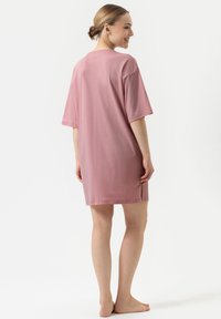 Camicetta da notte rosa corta realizzata in un tessuto morbido, con una vestibilità rilassata, maniche corte e orlo dritto, dotata di aperture laterali per facilitare i movimenti.