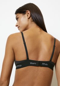 Zwart beha van een gladde, rekbare stof, met verstelbare bandjes en een haak-en-oog sluiting aan de achterkant. "Marc O'Polo" logo op de band.