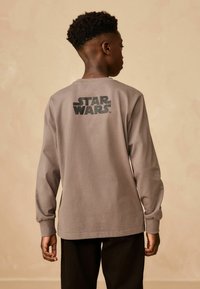 Szara bawełniana koszulka z długim rękawem z czarnym logo "STAR WARS" na plecach. Gładka tekstura, z prążkowanymi mankietami i okrągłym dekoltem.
