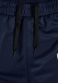 Granatowe spodenki sportowe z elastycznym pasem, czarnymi sznurkami zakończonymi srebrnymi końcówkami oraz gładką, teksturowaną tkaniną.