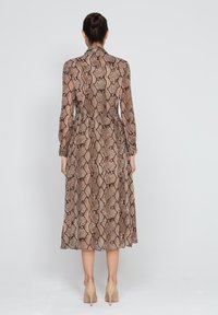 Długa, dopasowana sukienka w brązowy wzór w wężową skórę, z długimi rękawami, kołnierzykiem i swobodnym dołem. Wykonana z lekkiego materiału.